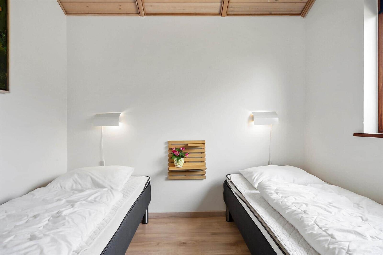 Zwei Einzelbetten mit weißen Bettwäsche stehen in einem Raum mit Holzdecke und Wandbeleuchtung.