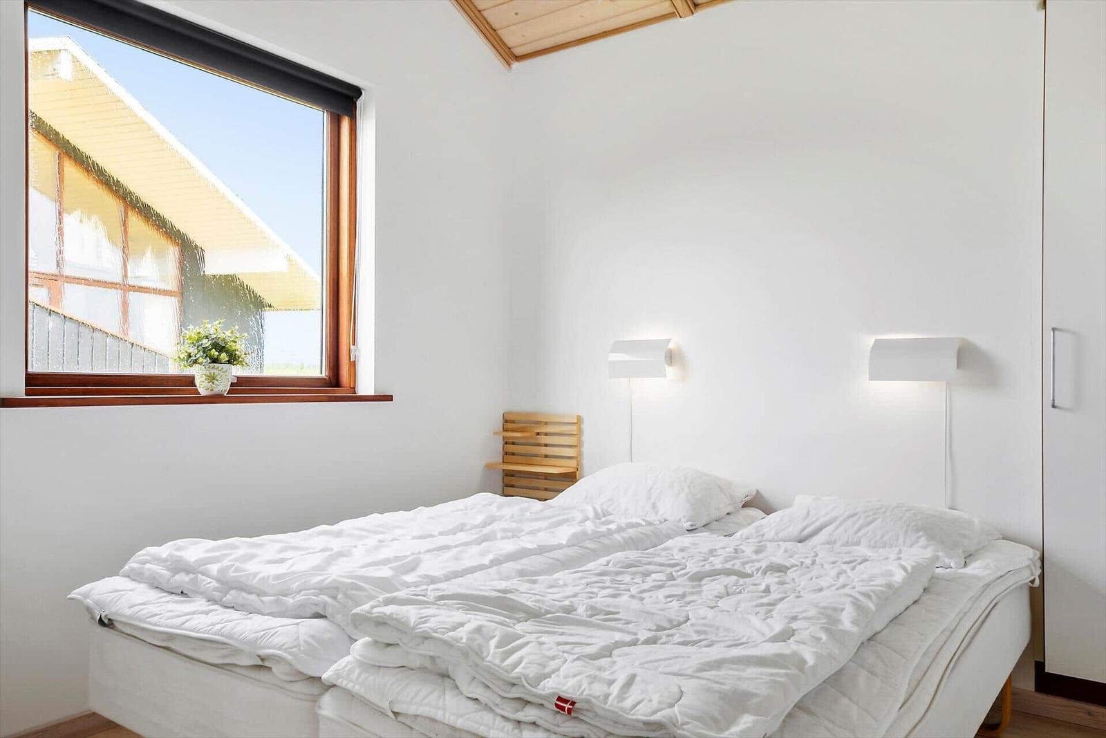 Schlafzimmer mit Doppelbett, Fenster und Wandlampen.