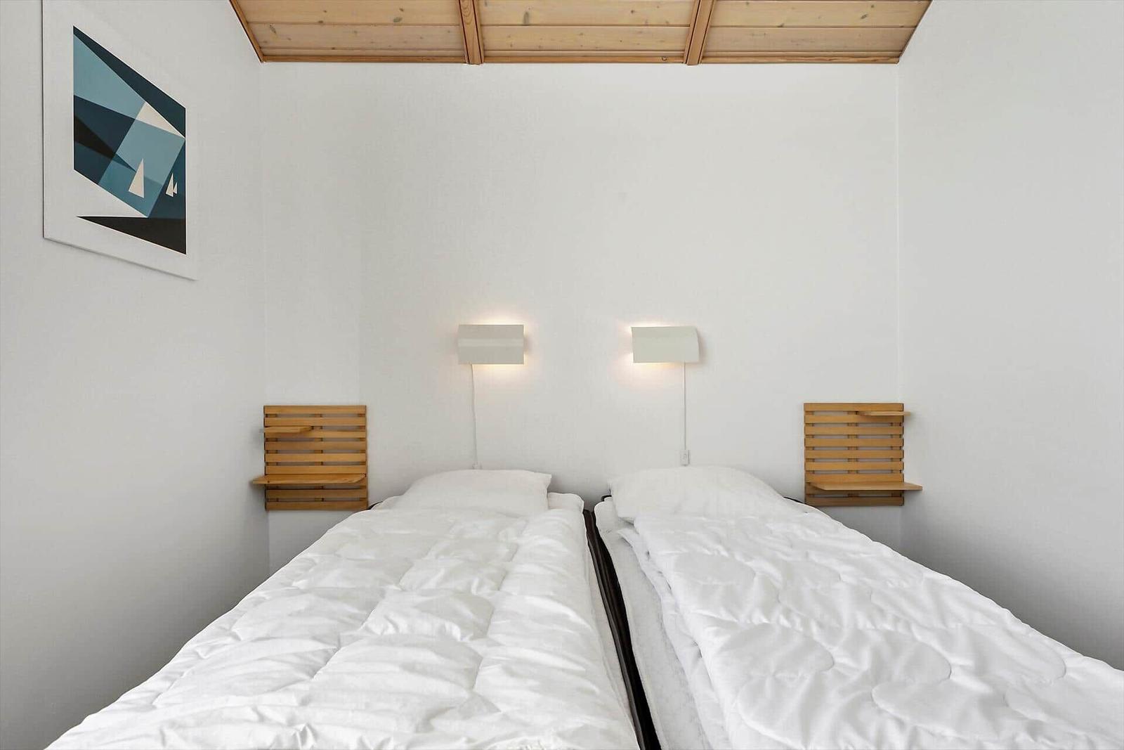 Zwei Betten mit weißen Bettwäschen, Holzregale und Wandlampen unter einem Holzdecken.