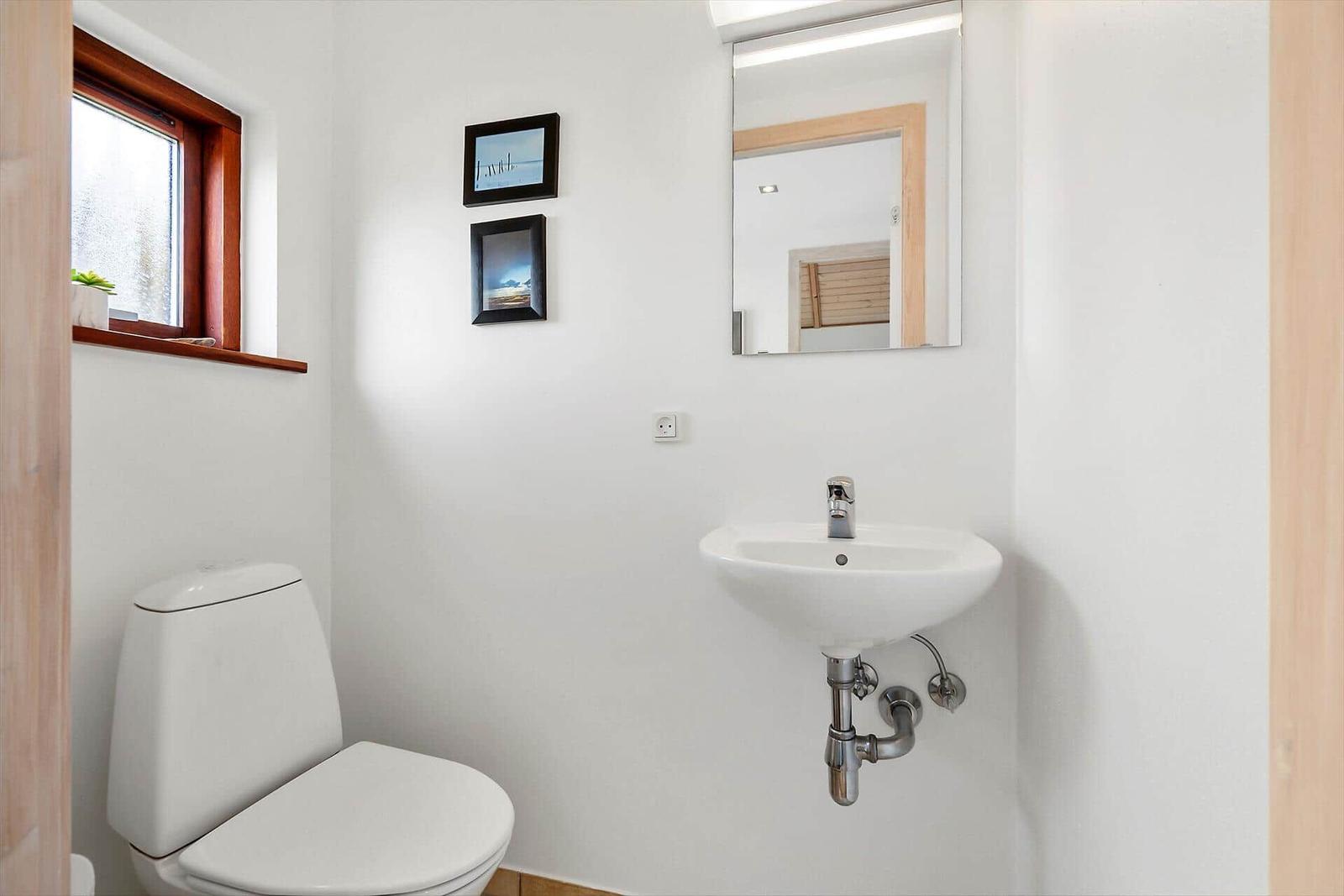 Badezimmer mit Toilette, Waschbecken und Spiegel. Fenster mit Holzrahmen.