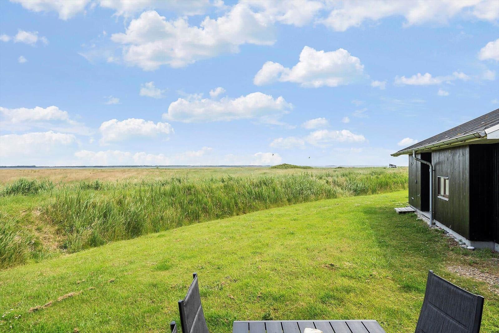 Grünes Grasfeld mit Blick auf Horizont. Holzhaus mit Tisch und Stühlen.