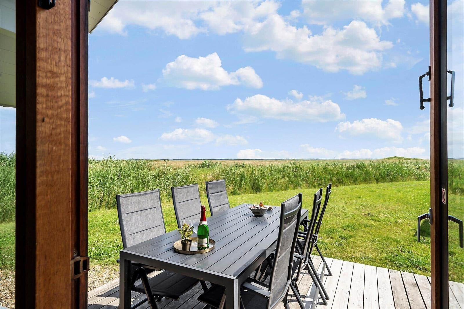 Terrasse mit Tisch und Stühlen bietet Blick auf Grasland und Himmel.