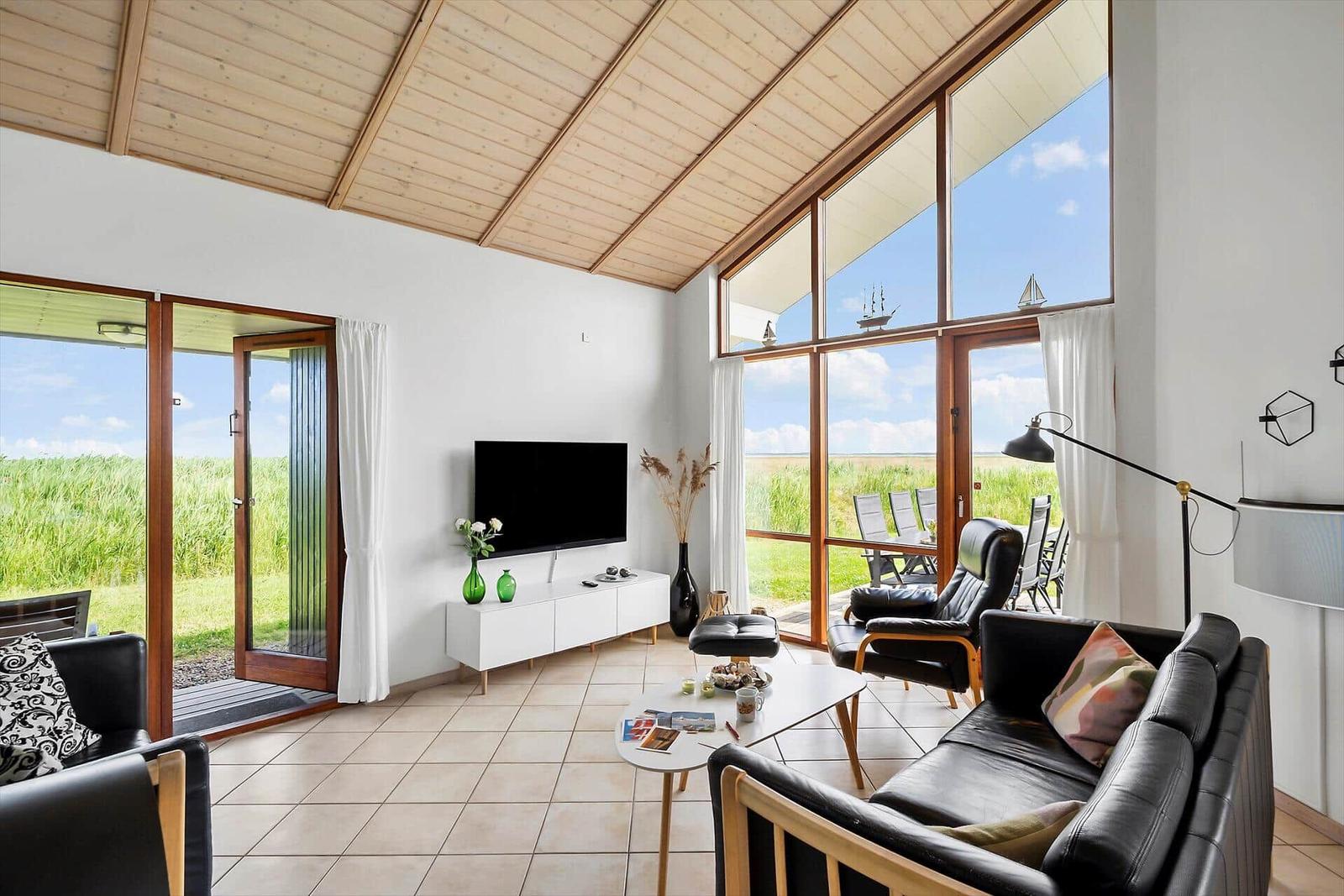 Wohnzimmer mit großem Fensterblick auf Grasland und Terrasse mit Sitzmöbeln.
