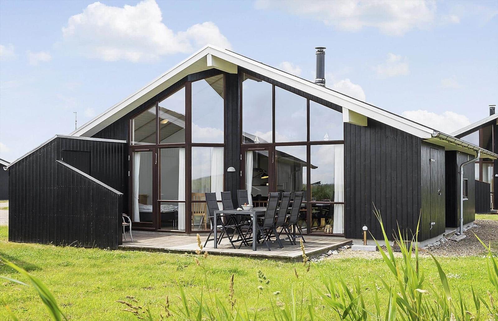Modernes Holzhaus mit großem Glasbereich und Terrasse mit Esstisch.
