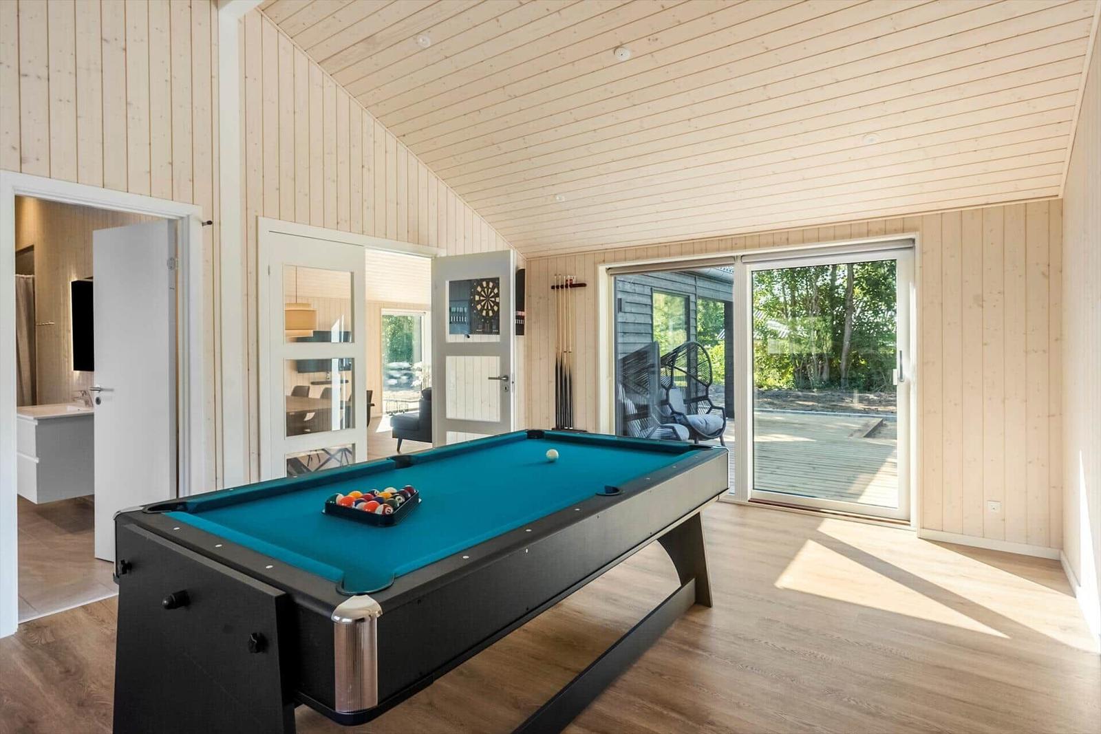 Room with pool table, wood walls, and glass door to outdoor area.