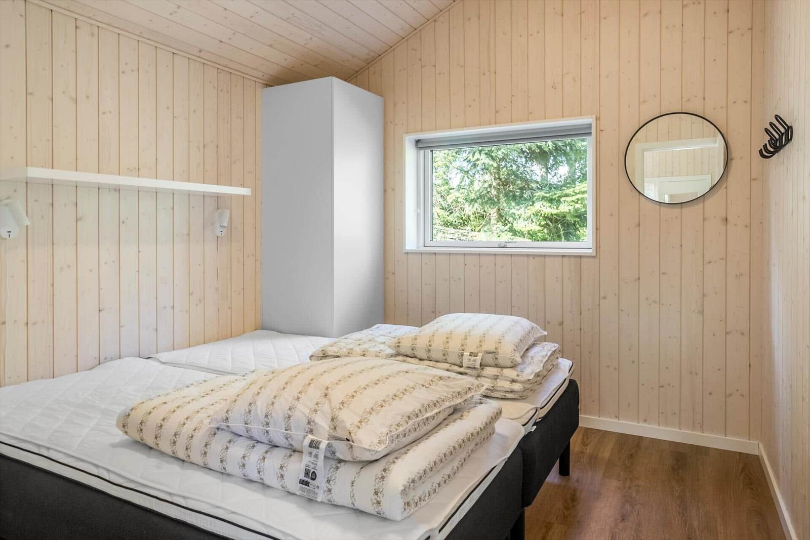 Bedroom with wooden walls, bed, window, and mirror