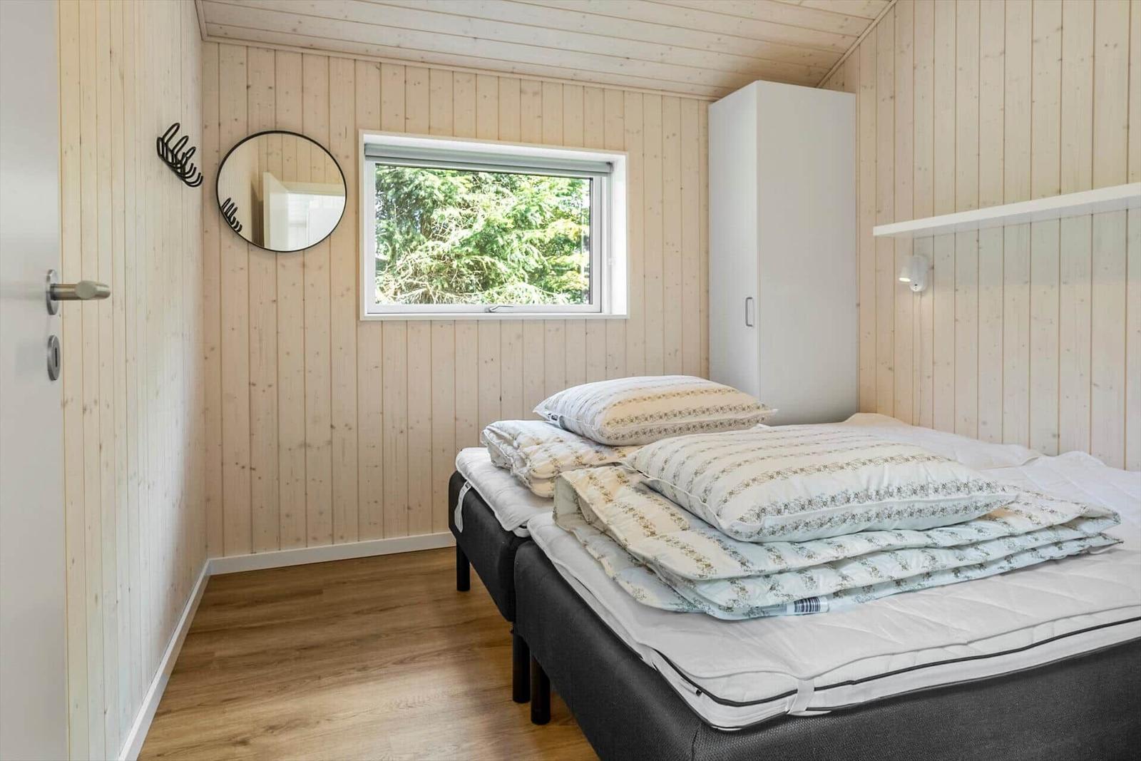 Bedroom with wooden walls, bed, and window to the forest.