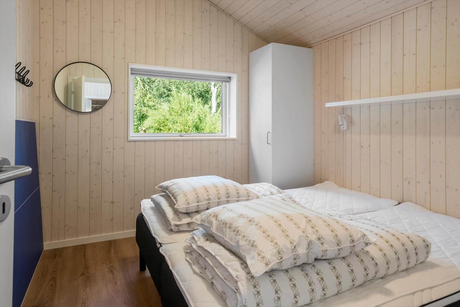 Bedroom with wooden walls, bed, window, and wardrobe.