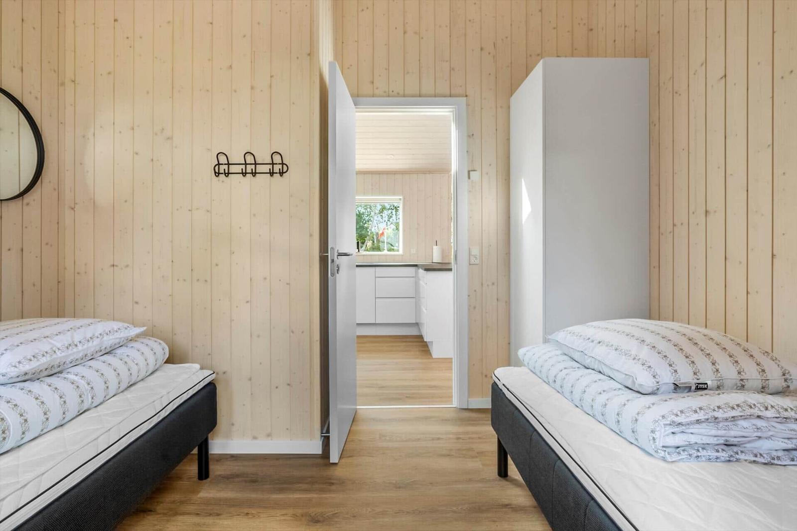 Two beds in a room with wooden walls and door to bathroom.
