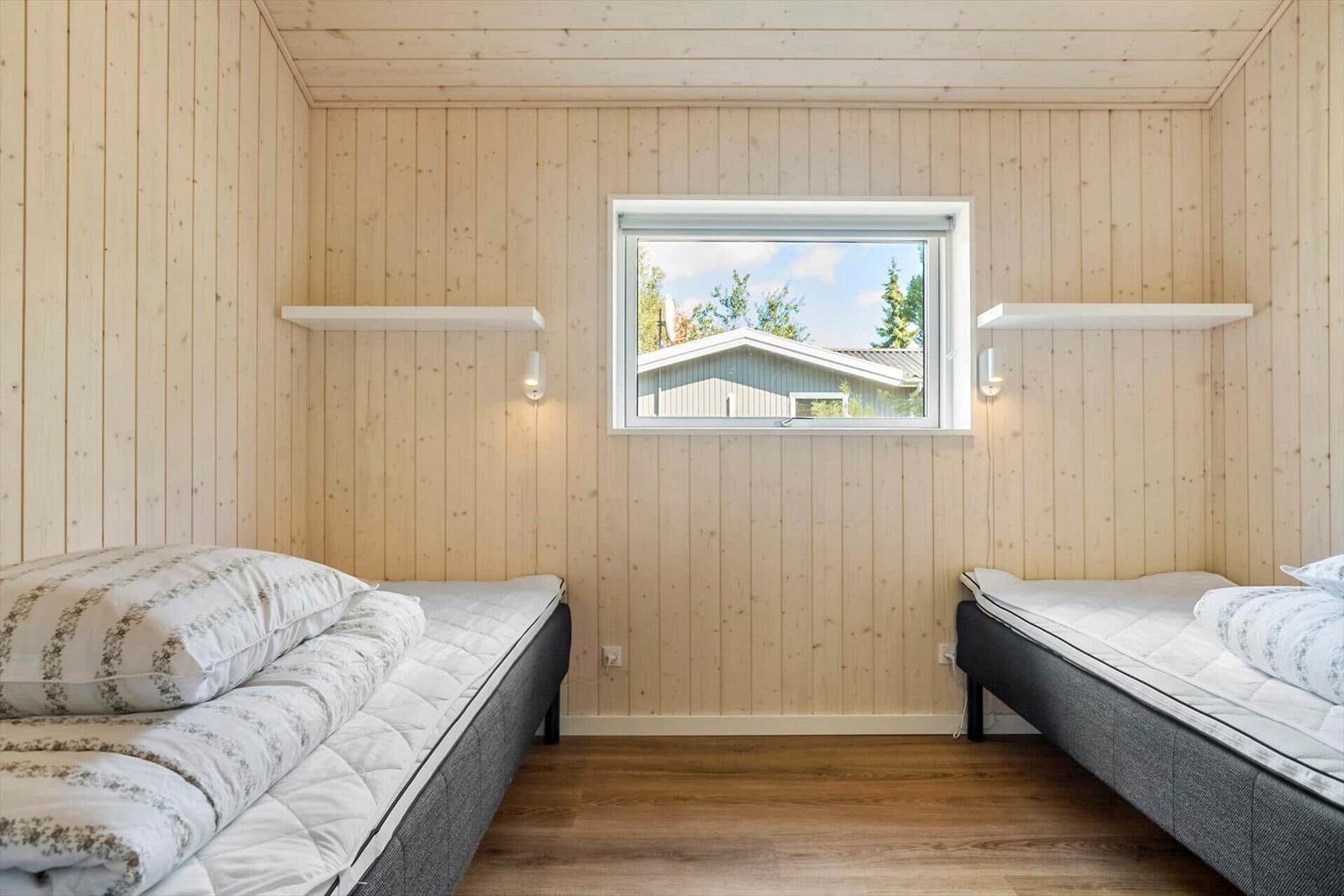 Two single beds in a room with wooden walls and a window.