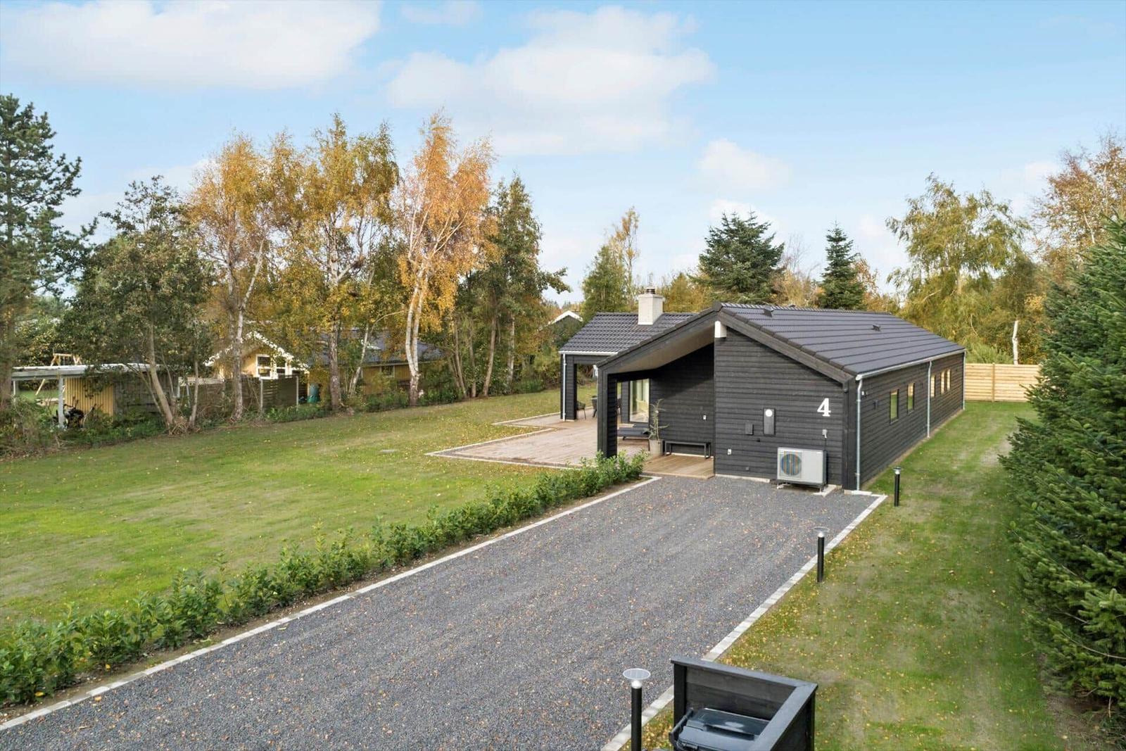 Modern villa with wooden veranda and garden. Green lawn and trees surround the house.