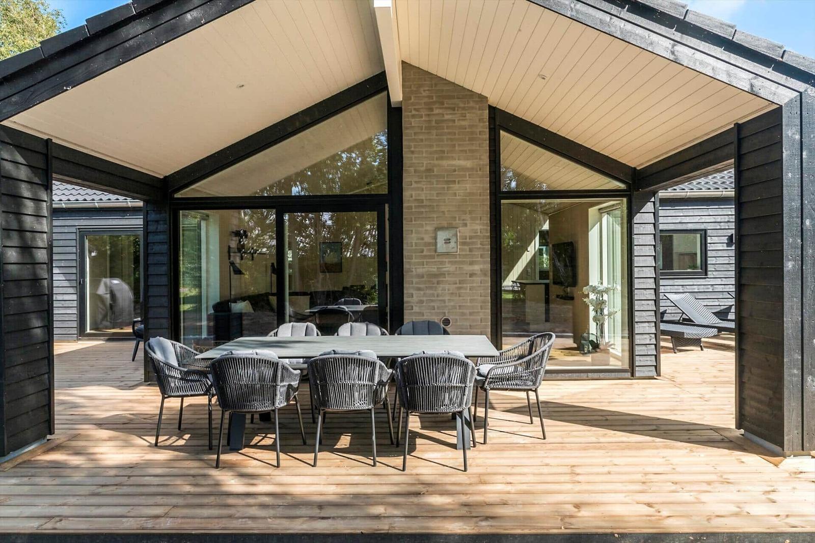 Deck with table and chairs under roof, glass walls and wooden floor.