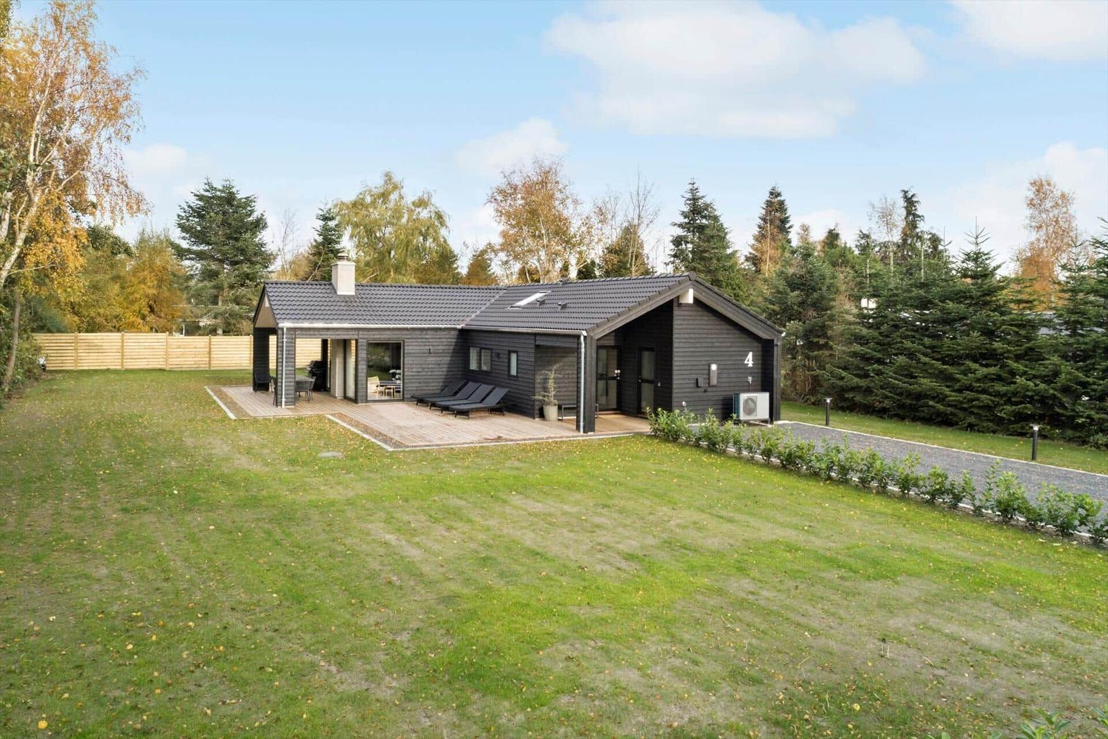 Modern villa with terrace, garden, and forest in the background.