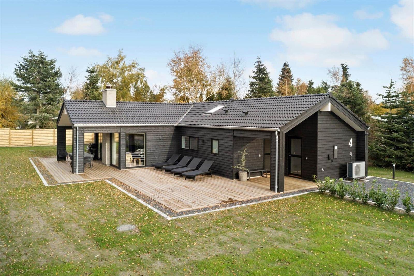 Modern villa with wooden terrace, sun loungers, and garden.