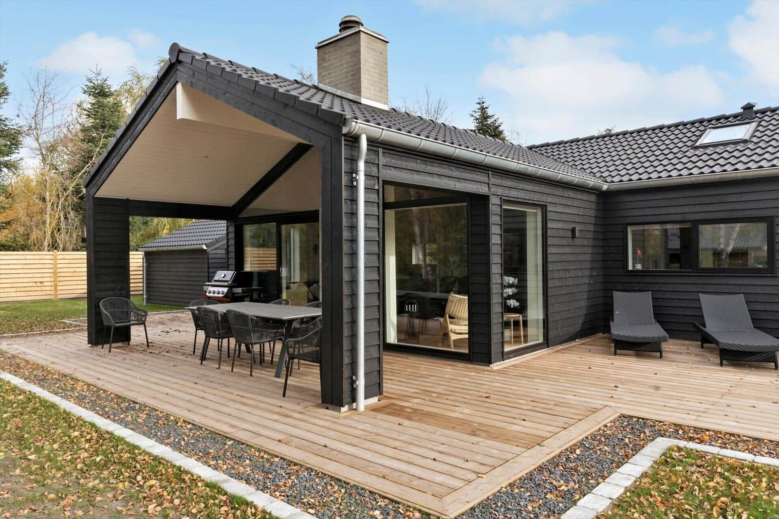 House with terrace, grill, and loungers. Wooden deck and black wood cladding.