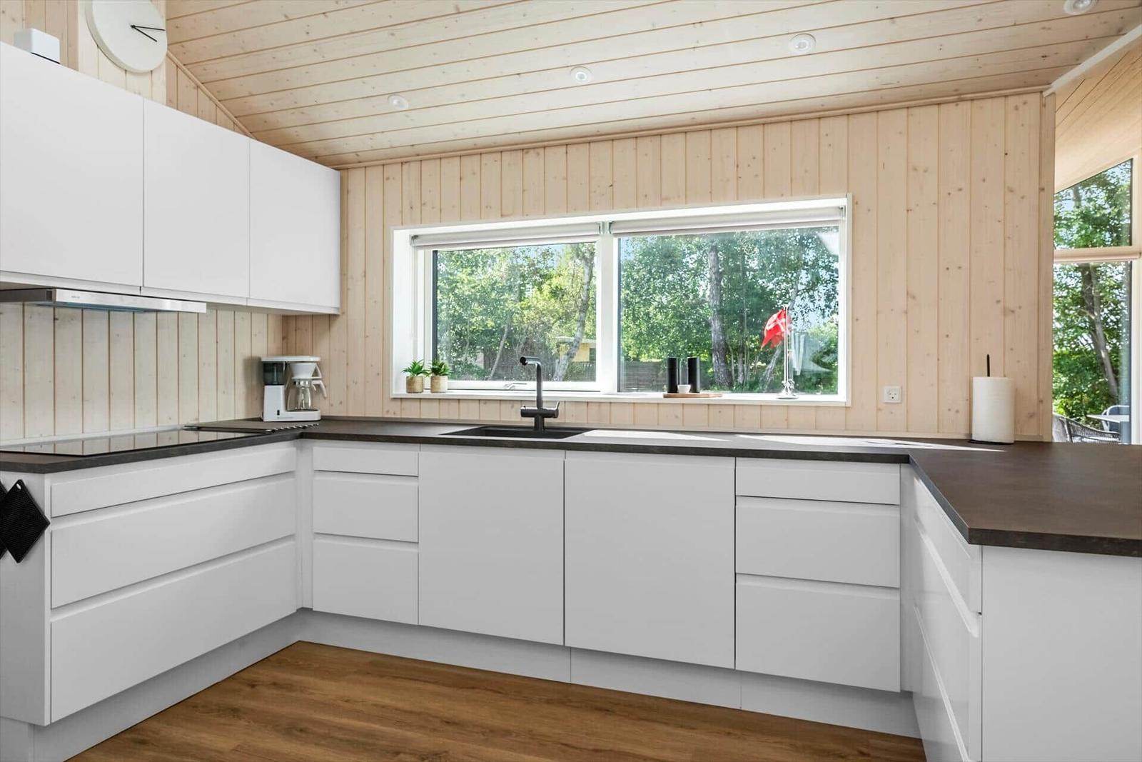 Kitchen with white cabinets, dark countertop, and wood paneling. Window with view of trees.