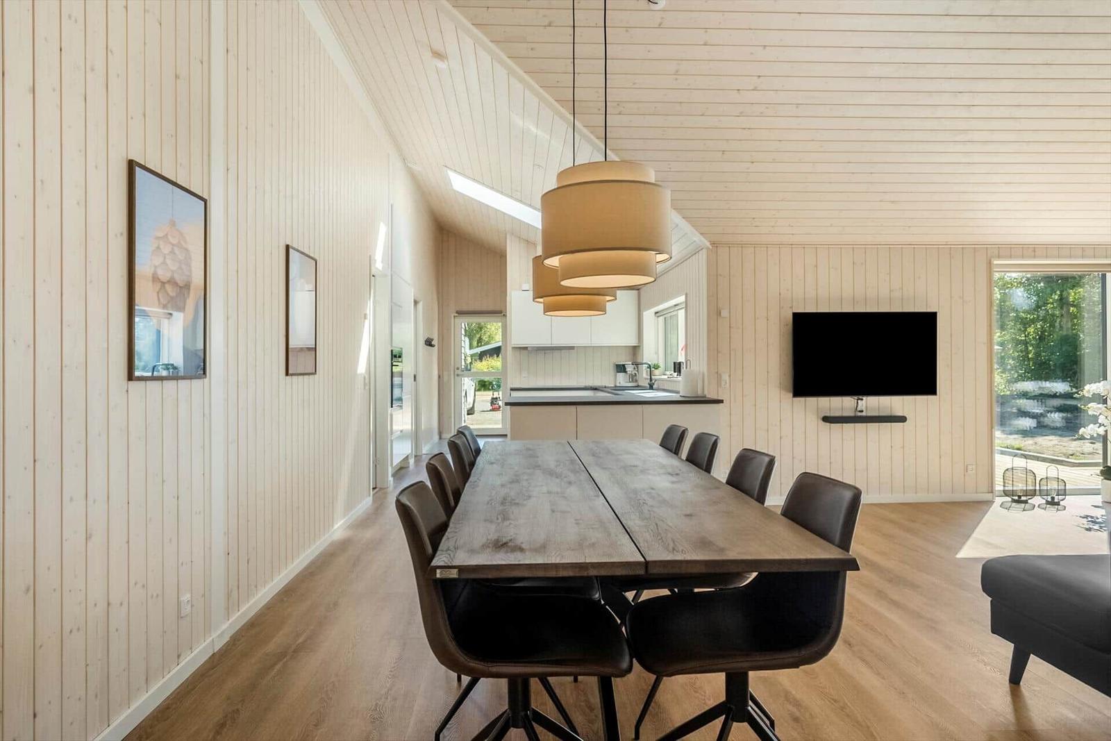 Large dining area with wooden table and chairs, kitchen area and TV wall.