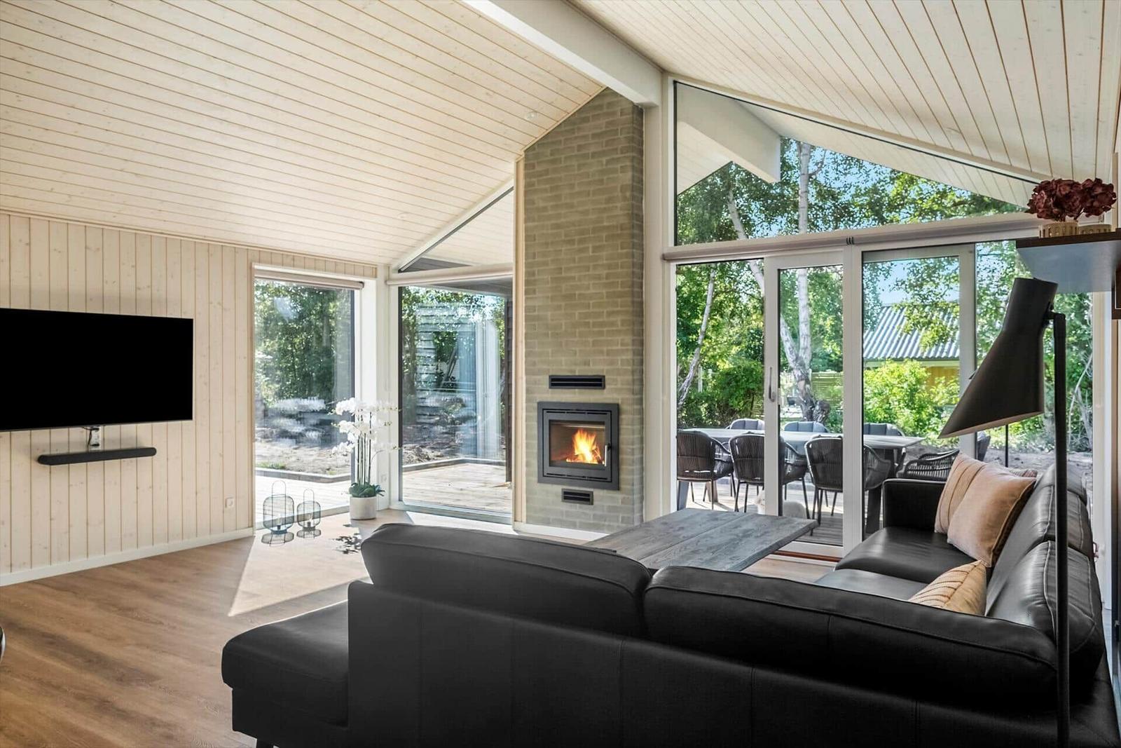 Living room with fireplace, sofa, and TV. Large windows with garden view.