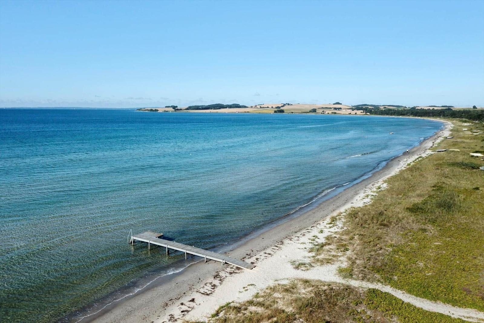 Beach with pier and clear water, landscape in the background.