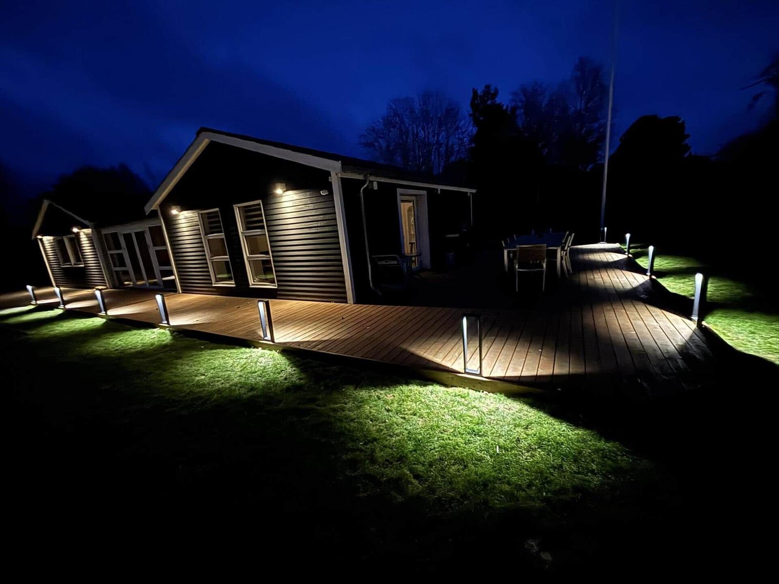 Hütte mit beleuchteter Terrasse und Grünfläche bei Nacht.