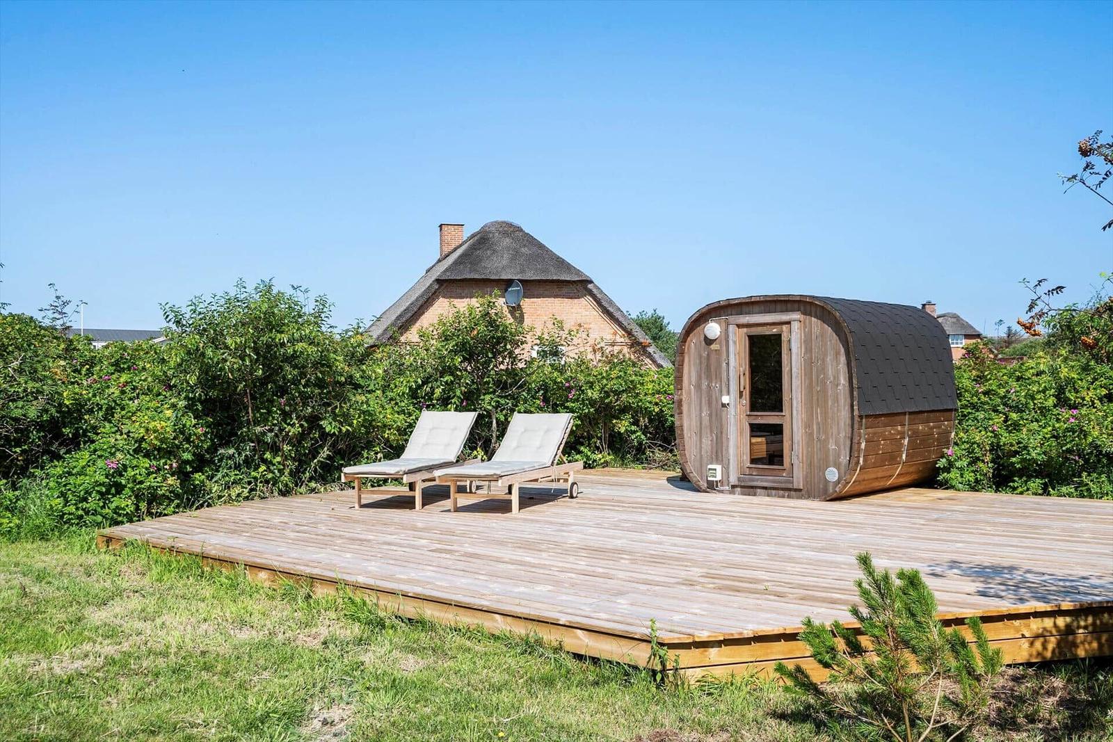 Holzterrasse mit Liegestühlen und Sauna neben einem Haus mit Schindeldach.