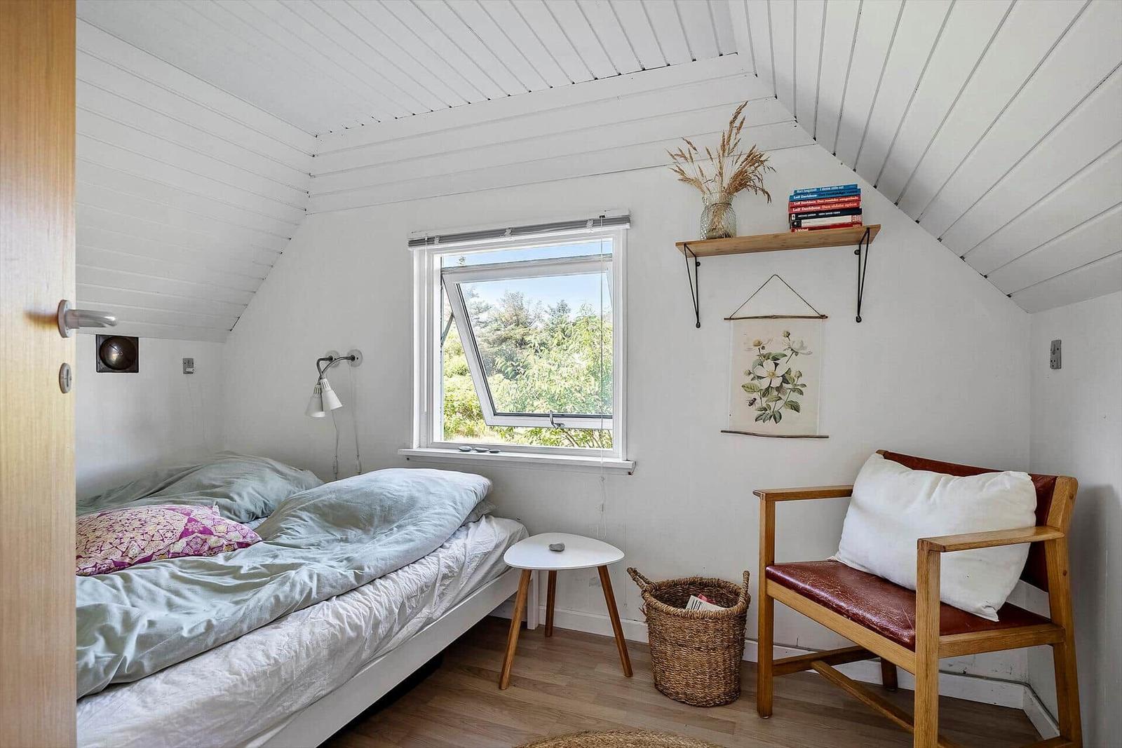 Schlafzimmer mit Bett, Stuhl und Fenster. Decke ist schräg und weiß.