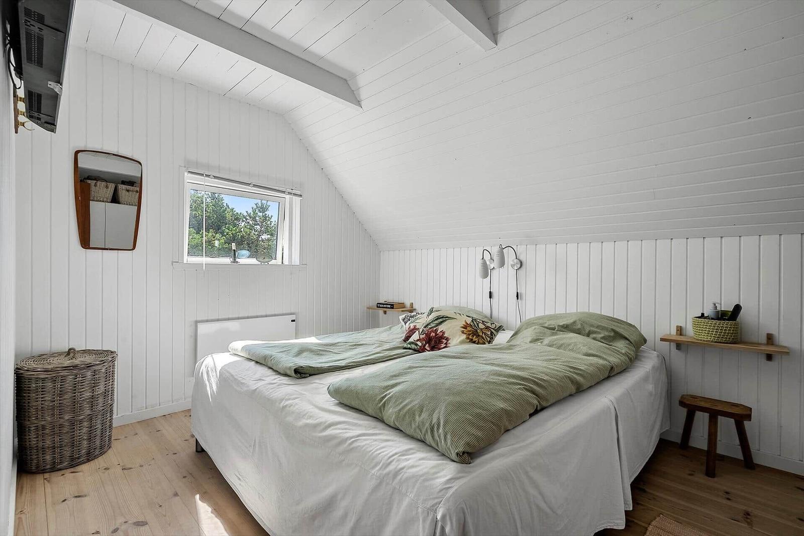 Schlafzimmer mit Bett, Fenster und weißen Wänden.