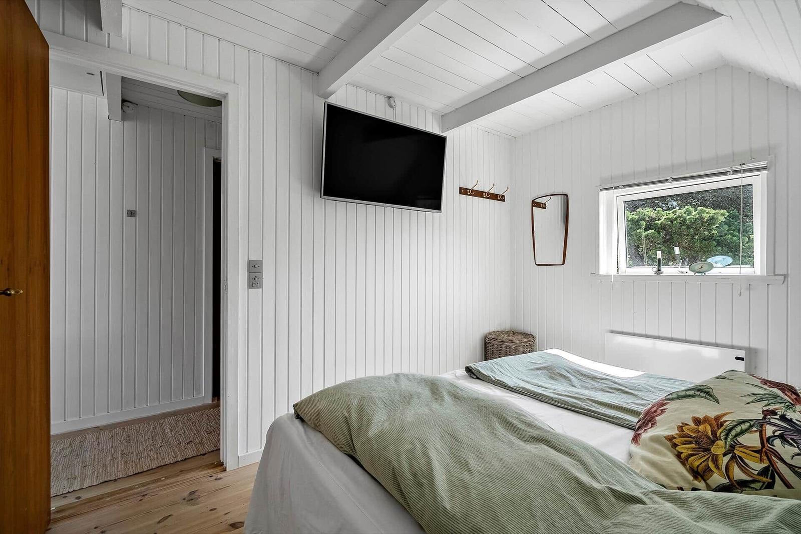 Schlafzimmer mit Bett, TV und Fenster mit Blick auf Grün.