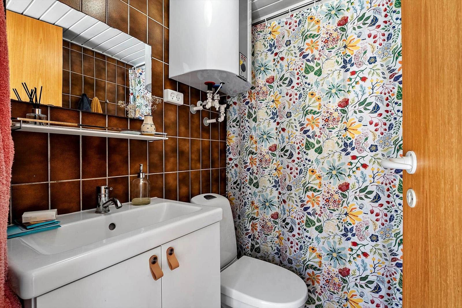Badezimmer mit Waschbecken, Toilette und blumigem Duschvorhang.