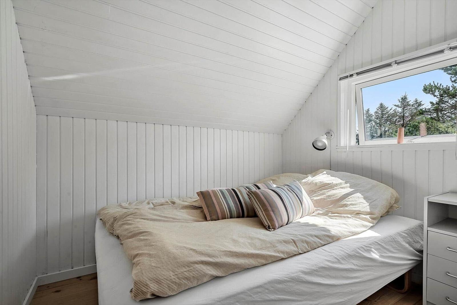 Schlafzimmer mit Bett, Fenster und weißen Wänden.
