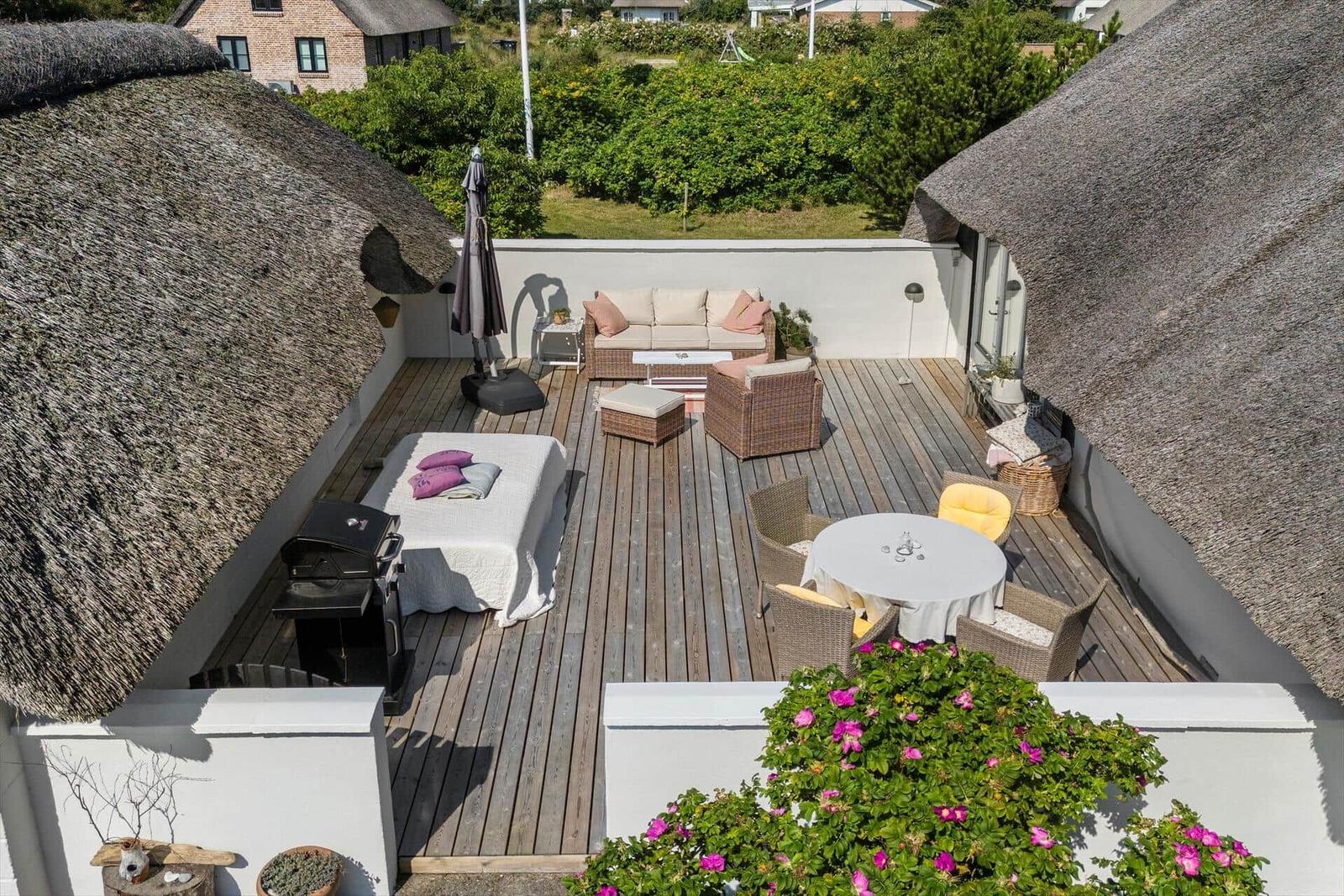 Terrasse mit Sitzgruppe, Tisch, Grill und Blick auf Grünflächen.