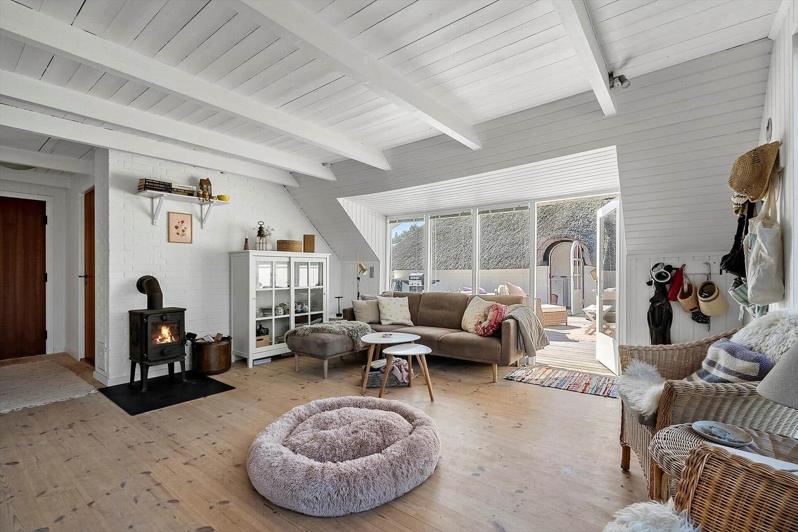 Wohnzimmer mit Kamin, Sofa und Rattanmöbeln. Holzboden und weiße Wände.