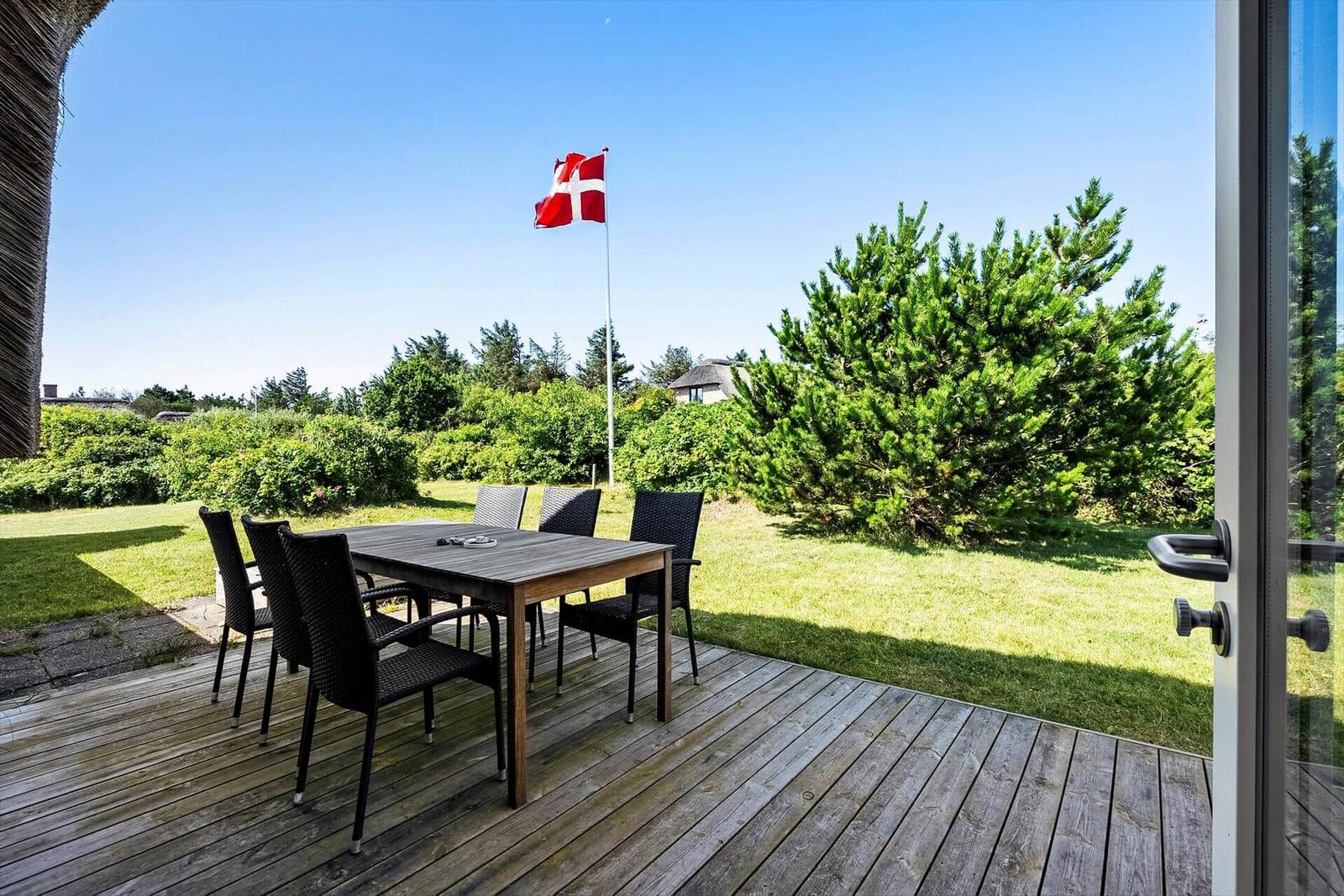 Terrasse mit Tisch und Stühlen, Blick auf Grünfläche und dänische Flagge.