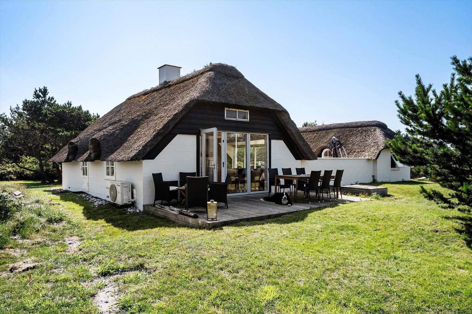Haus mit Strohdach, Terrasse und Garten. Ein Hund liegt auf der Terrasse.