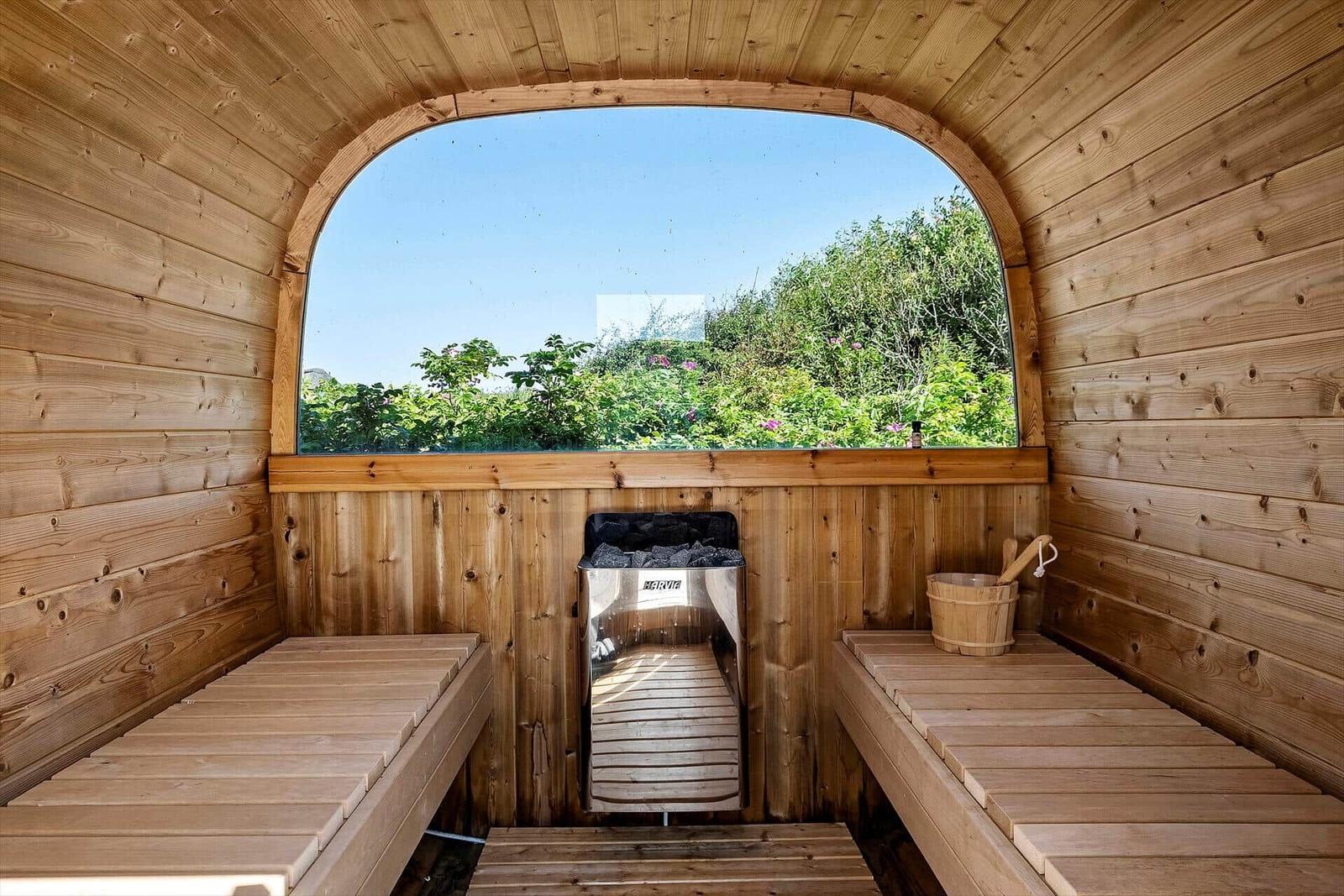 Holzsauna mit Sitzbänken und großem Bogenfenster zur grünen Außenaussicht.
