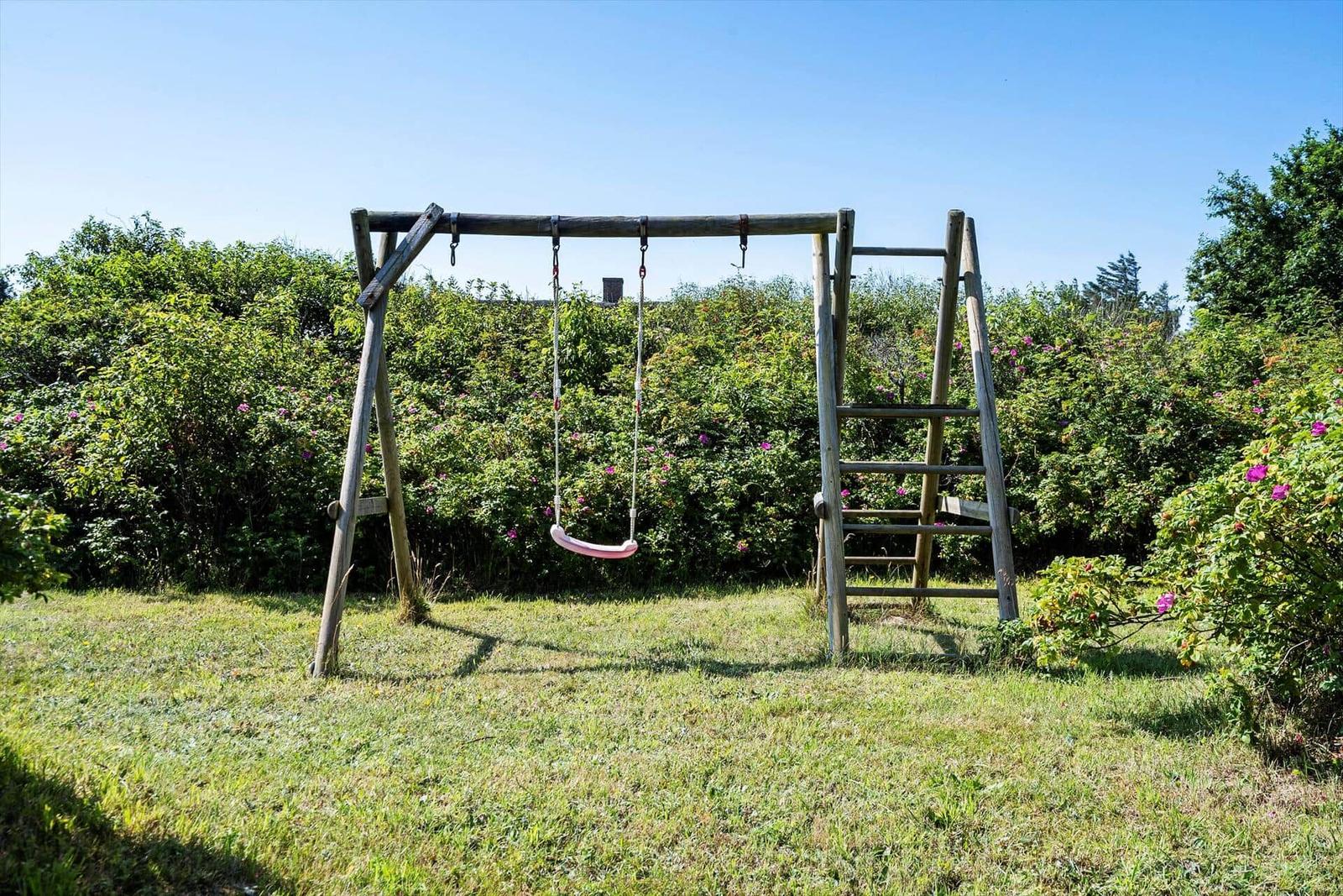 Holzschaukel mit Leiter im Garten mit grünem Rasen und Sträuchern.