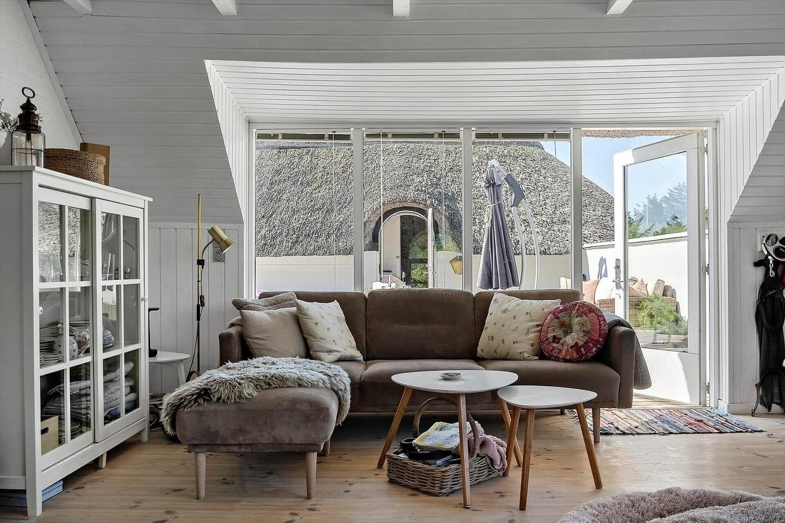 Ein Wohnzimmer mit braunem Sofa, Glaswand und Blick auf einen Garten.