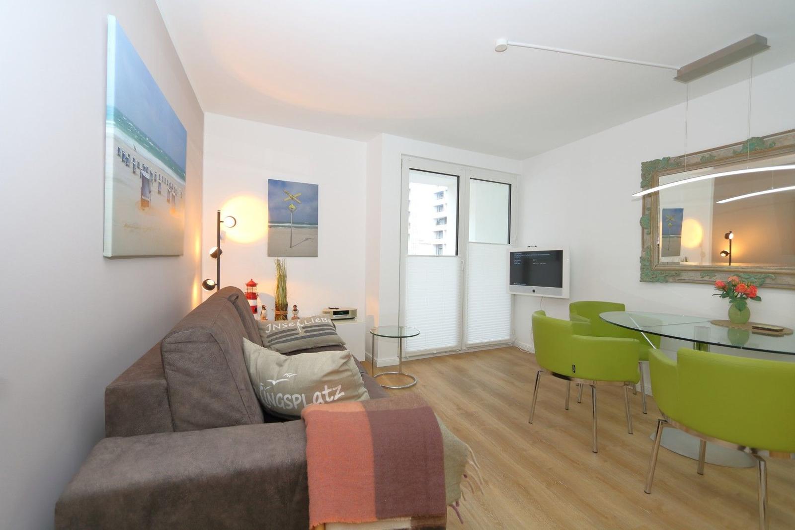 Wohn- und Essbereich mit Sofa, grünen Stühlen und Glas-tisch.