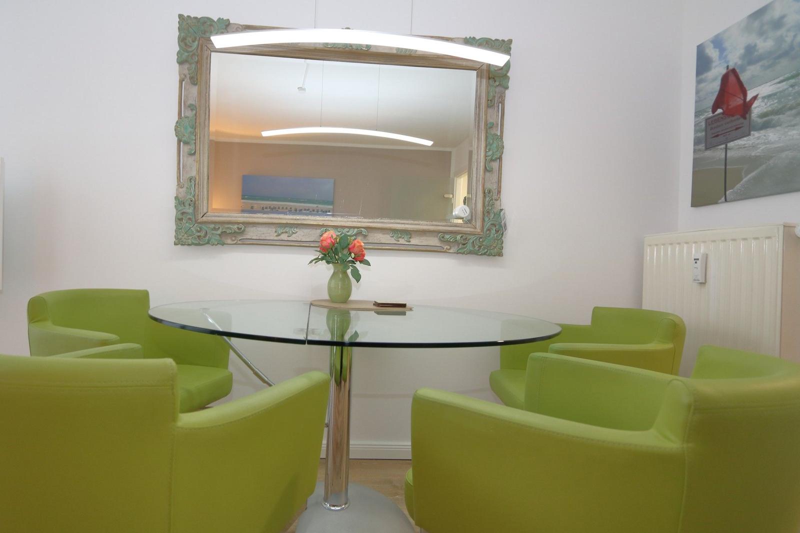 Runder Tisch mit grünen Stühlen, Spiegel und Blumen.