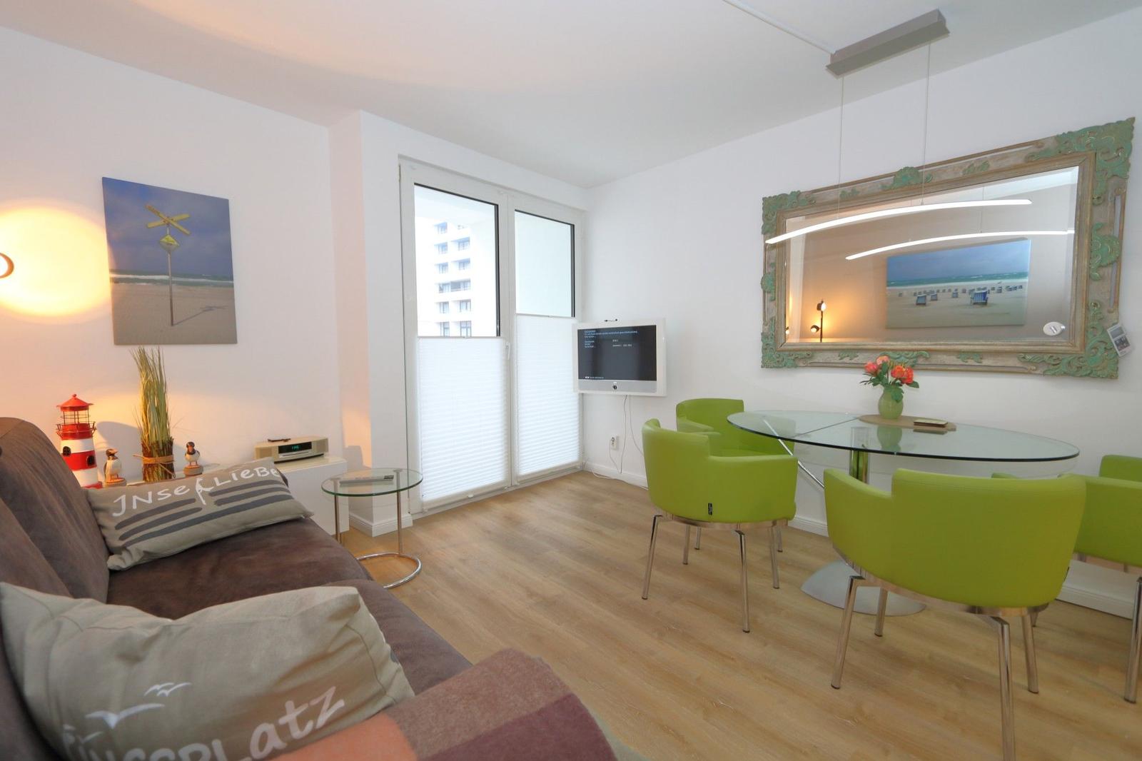 Wohn- und Essbereich mit grünen Stühlen, Glas-Tisch und Fernseher.
