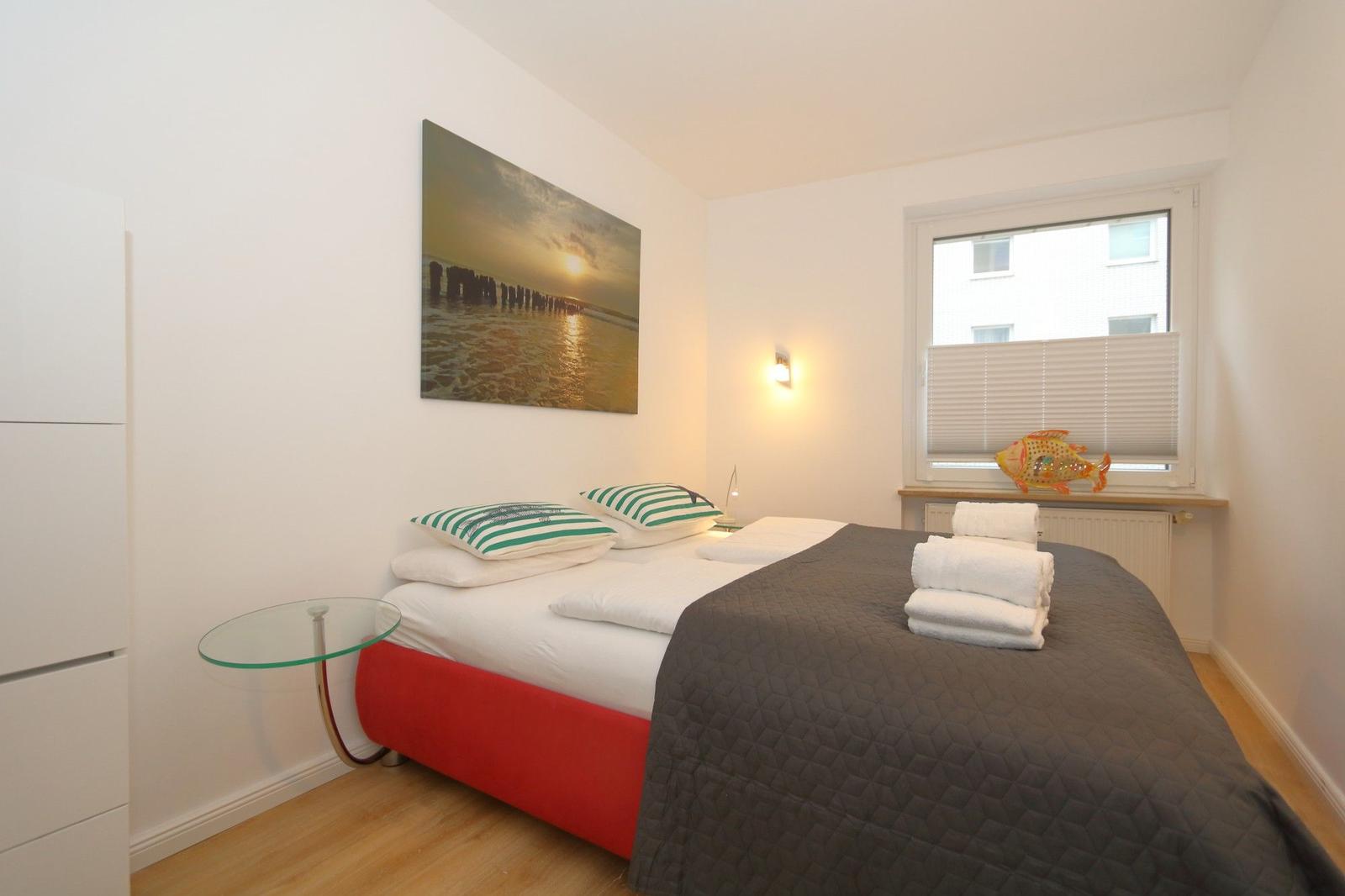 Schlafzimmer mit Bett, Wandbild und Fenster mit Jalousie.