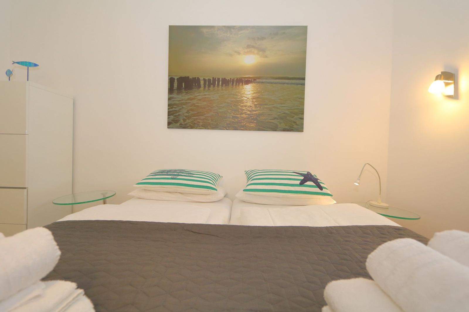 Schlafzimmer mit Bett, Kissen und Wandbild. Neben dem Bett stehen Nachttische mit Lampen.