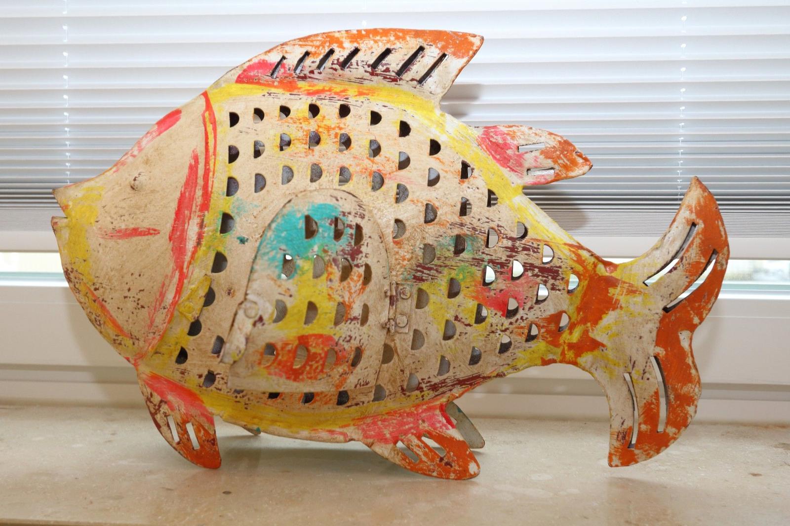 Farbenfroher Fisch aus Metall mit Lochmuster steht auf einer Fensterbank.