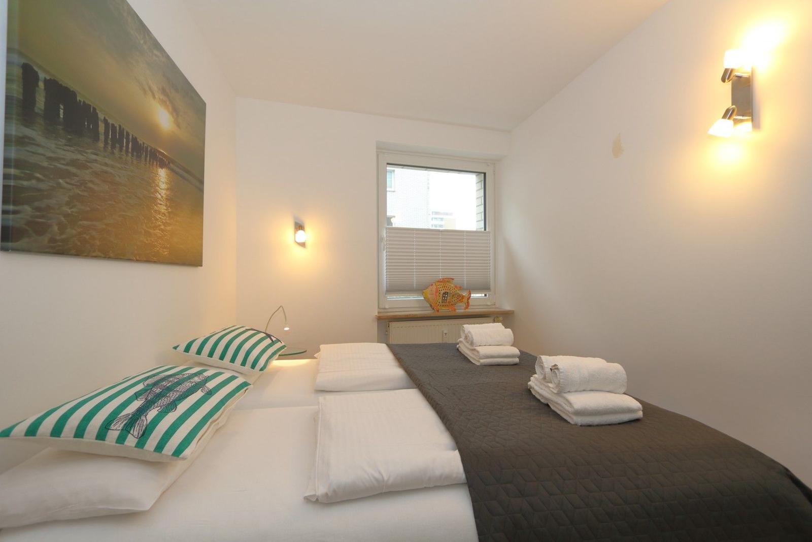 Schlafzimmer mit Bett, Wandbild und Fenster mit Jalousie.