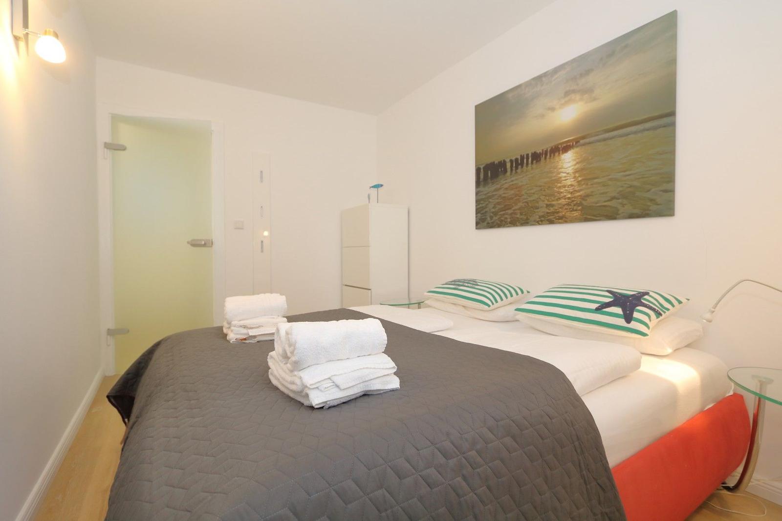 Schlafzimmer mit Bett, Kissen und Wandbild. Handtücher auf dem Bett.