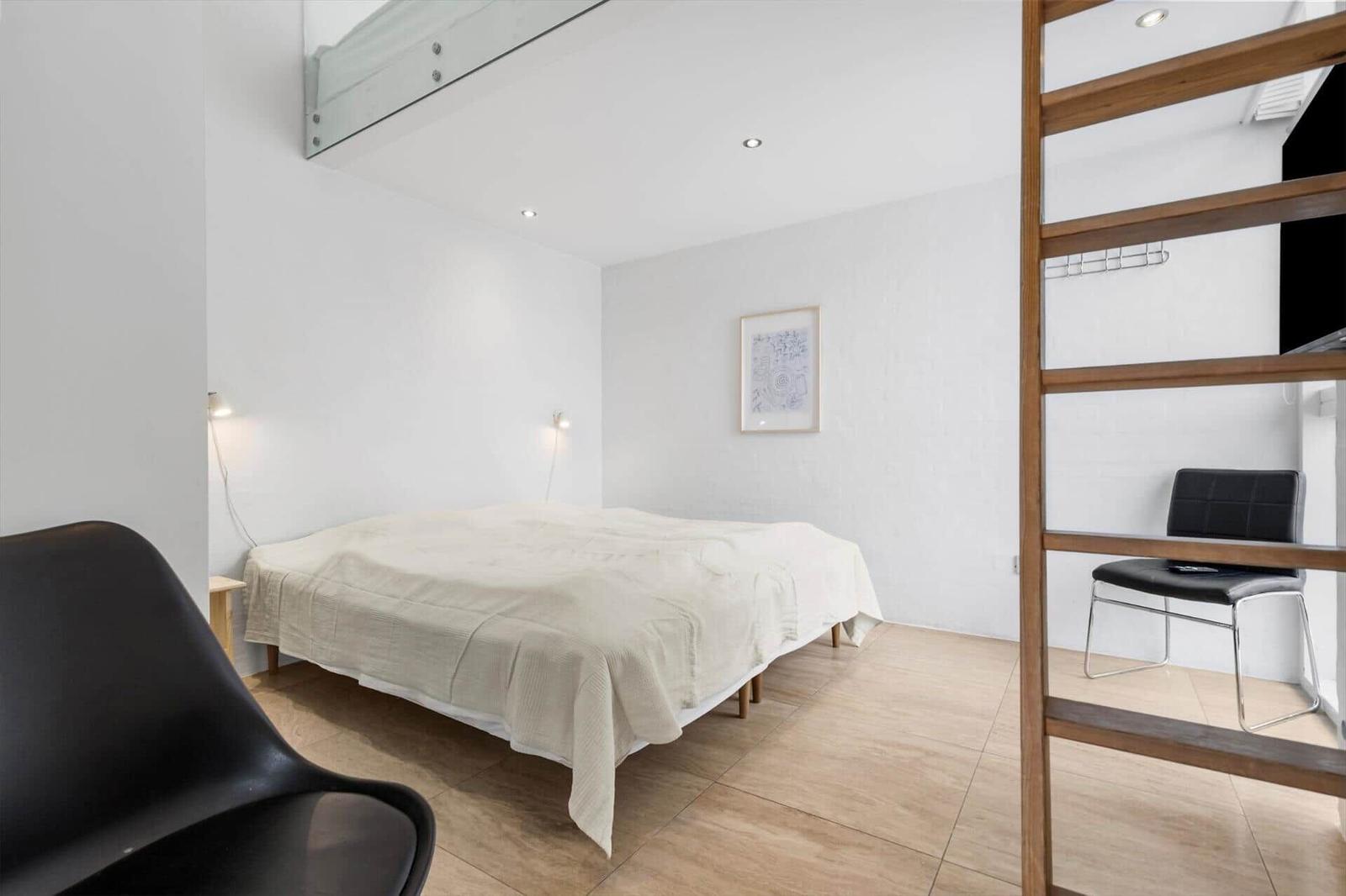 Schlafzimmer mit Bett, Wandbild und Holzboden. Holzleiter führt zu einem Aufstellbereich.