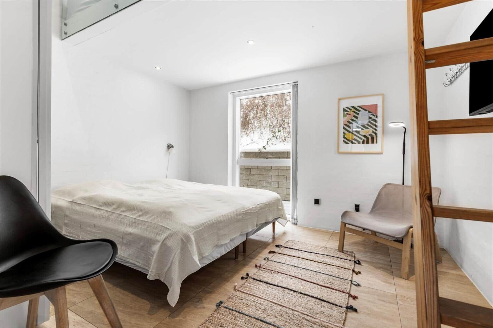 Schlafzimmer mit Bett, Stuhl und Fenster. Holzfußboden und Teppich.