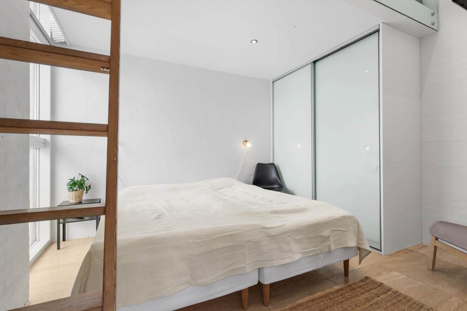 Schlafzimmer mit Bett, Schwebetüren und Pflanze am Fenster