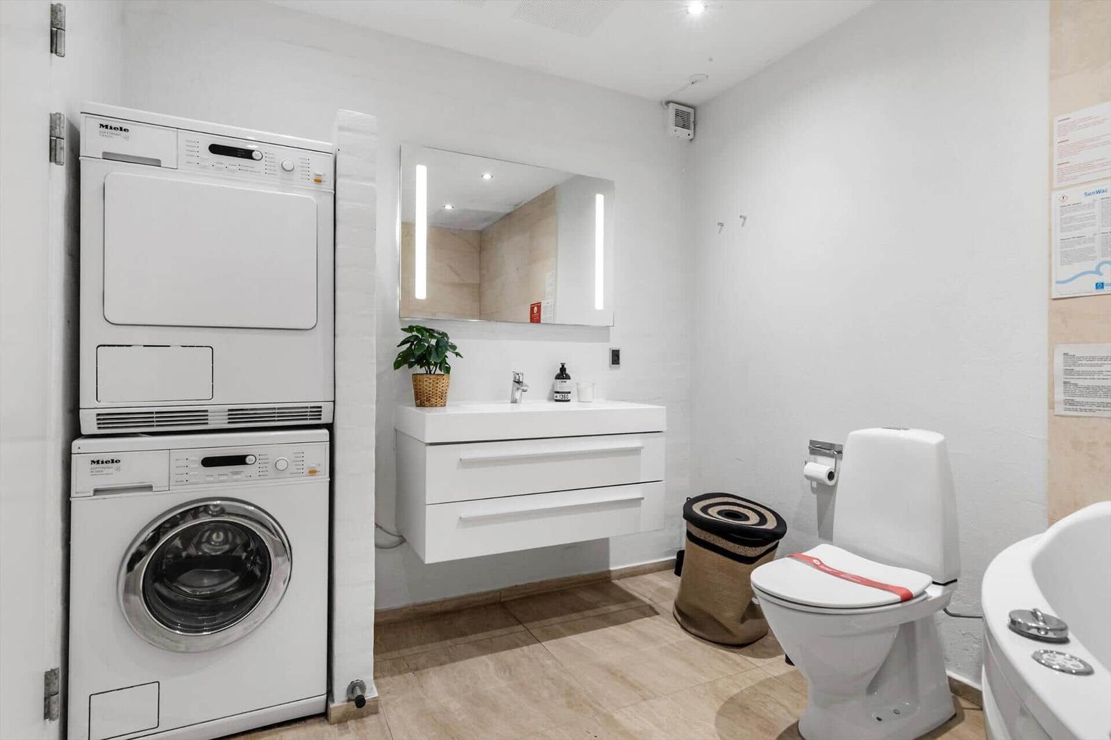 Badezimmer mit Waschmaschine, Trockner, Waschtisch und Toilette.