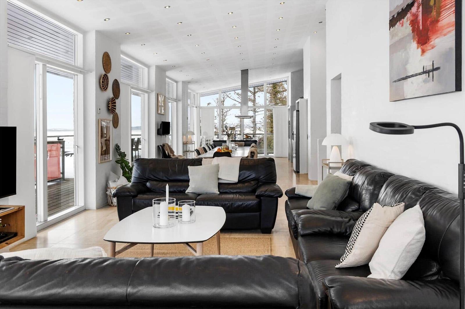 Wohnbereich mit Ledersofas, Glasfronten und Essbereich im Hintergrund.